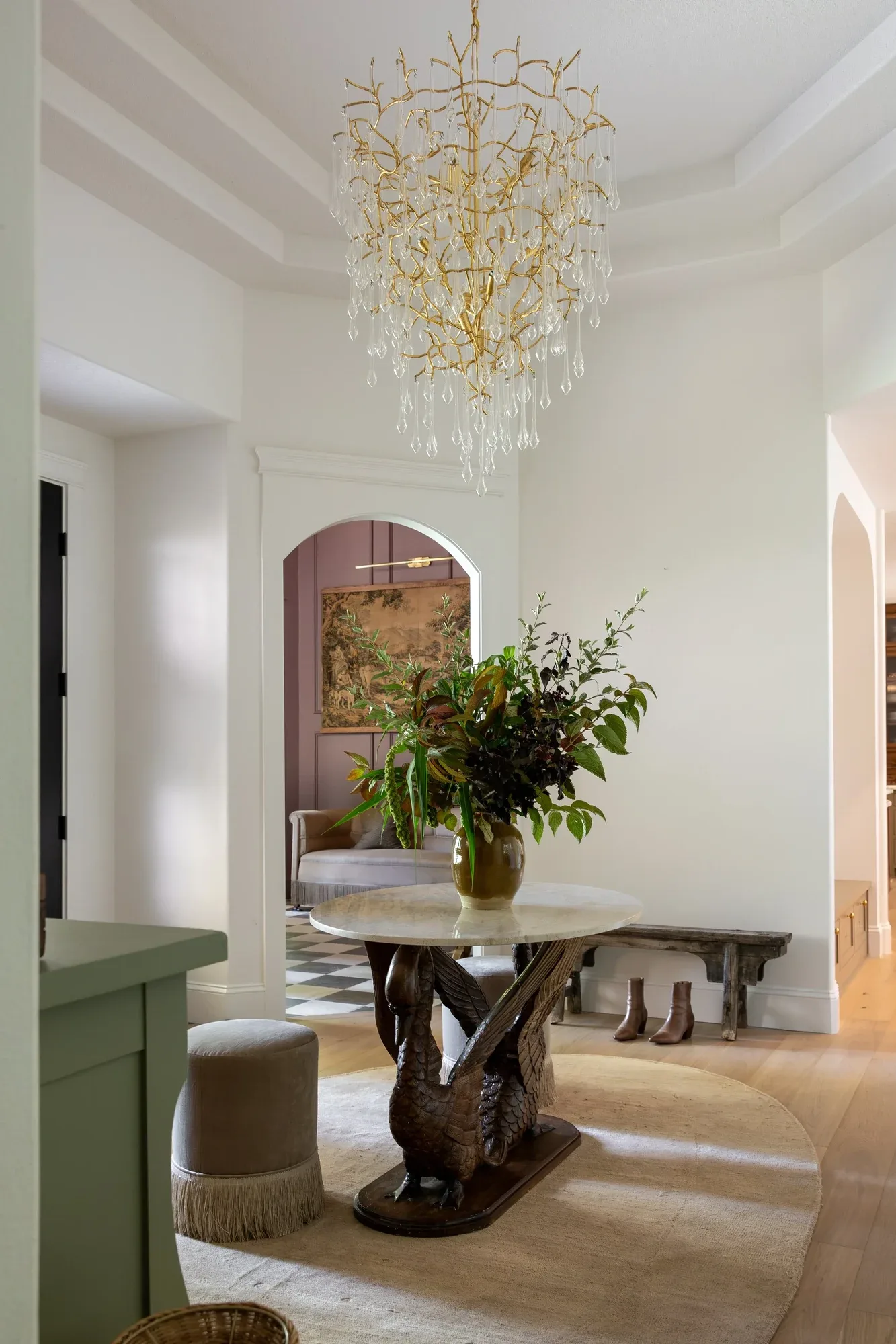 A garden arrangement on a sculptural round table in a foyer, beneath a gilded chandelier