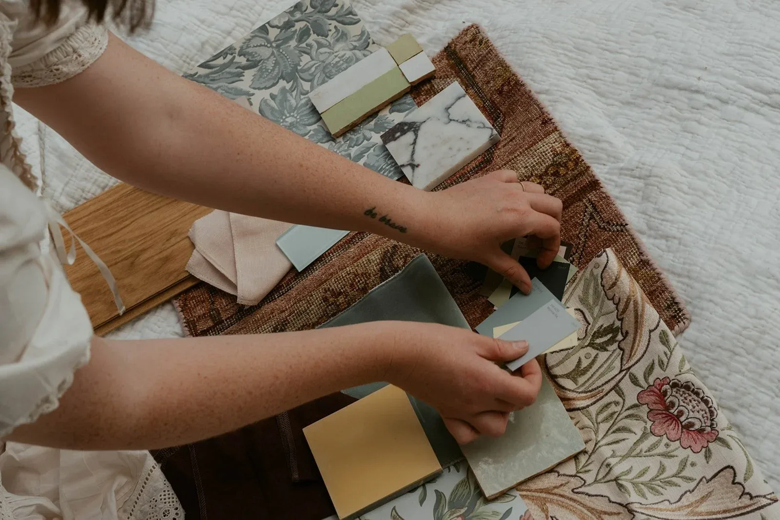 Hands arranging fabric, tile and wallpaper samples on a woven rug