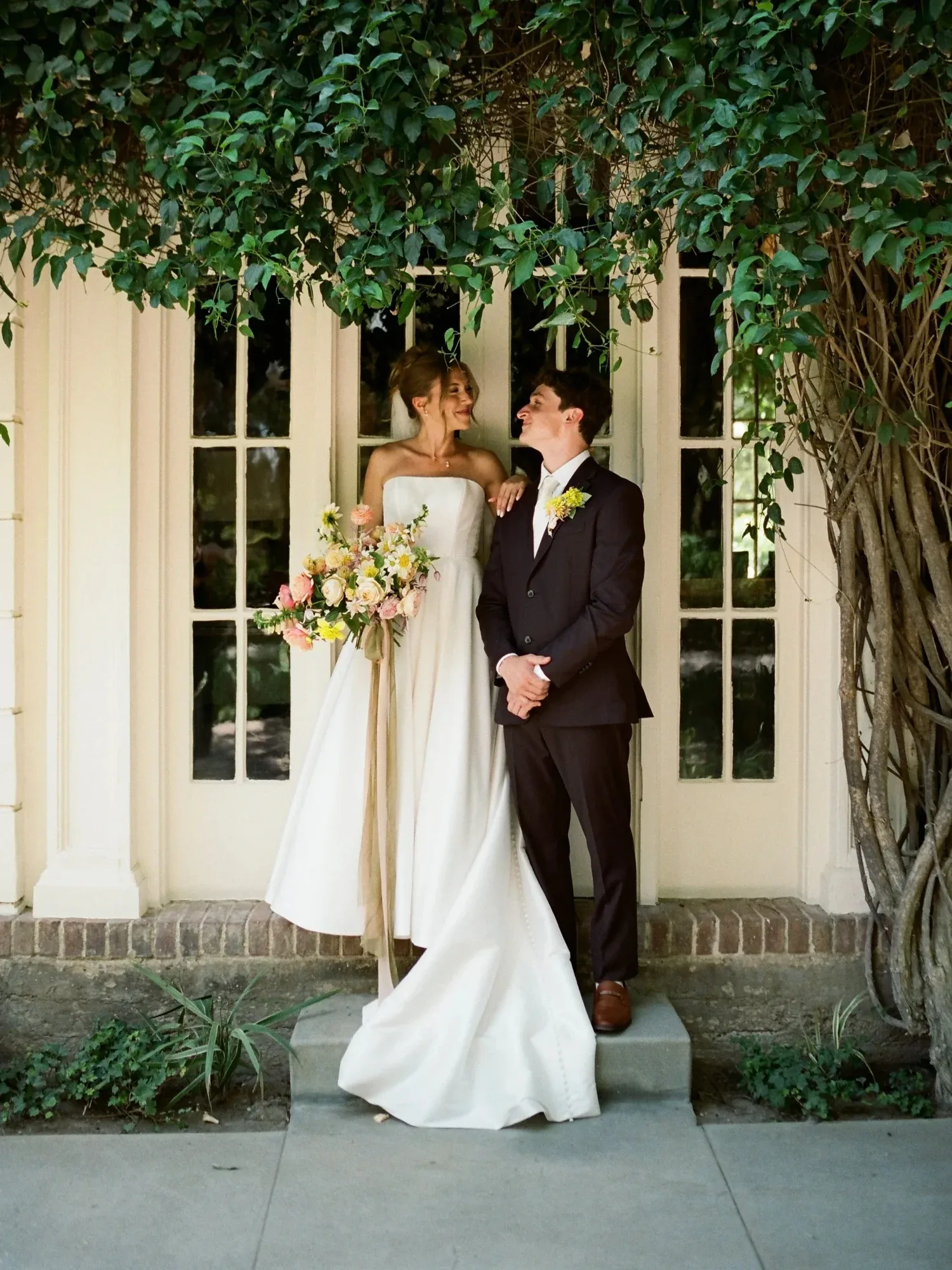 A couple beneath a canopy of vines at a garden doorway, the bride holding a bouquet
