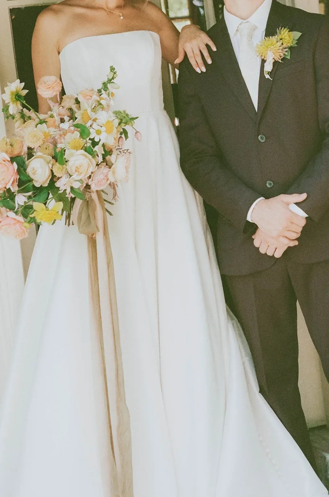 A bride holding a loose, ribboned bouquet beside her partner
