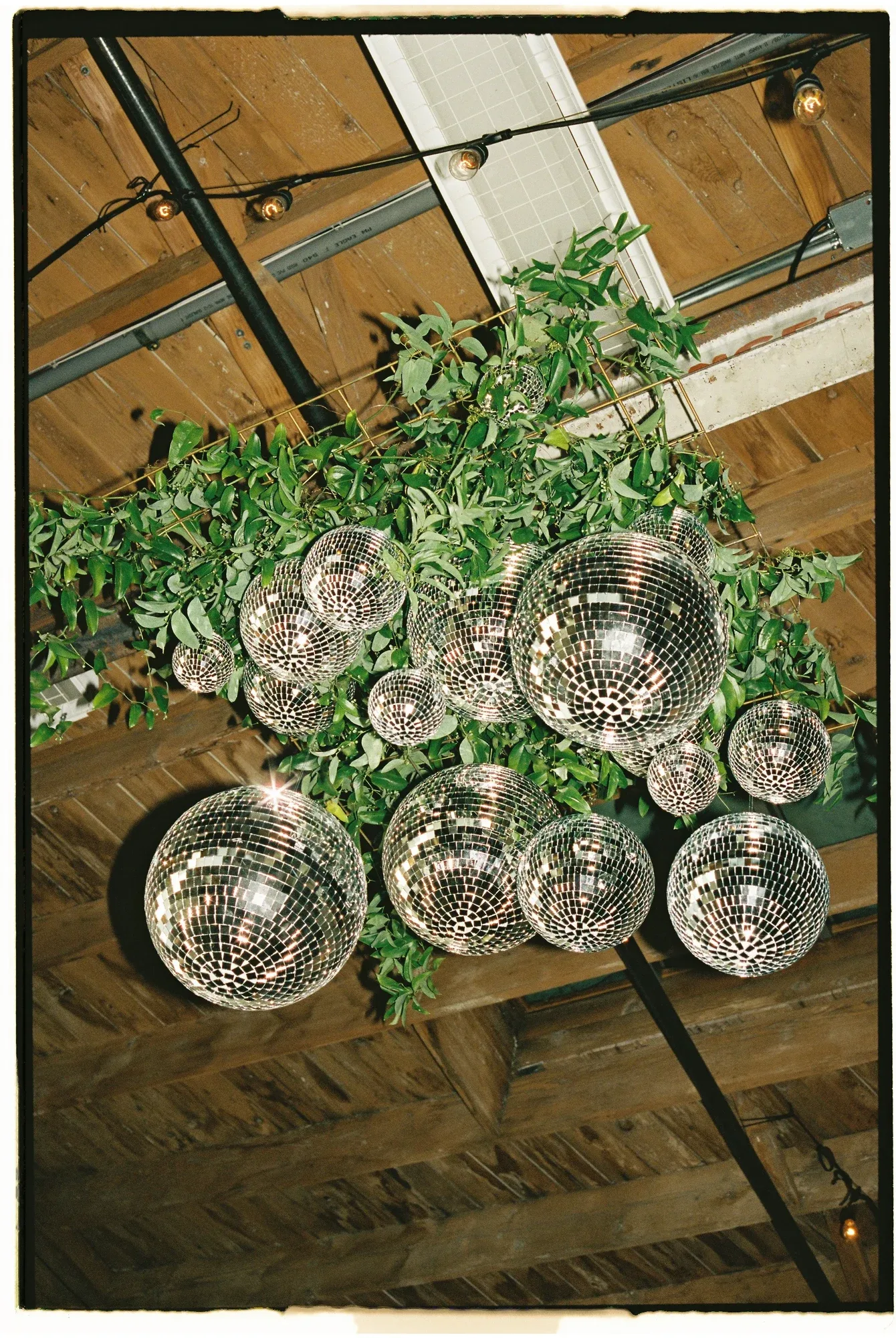 A suspended installation of greenery and mirror balls beneath a timber ceiling