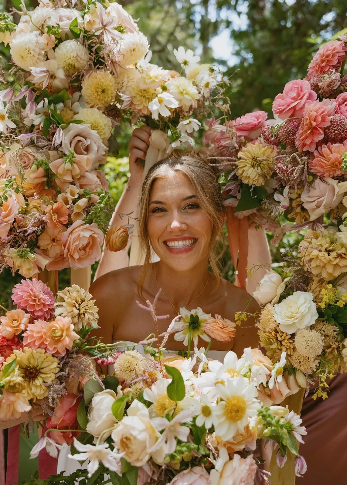 A smiling bride framed by an abundant arch of dahlias and roses