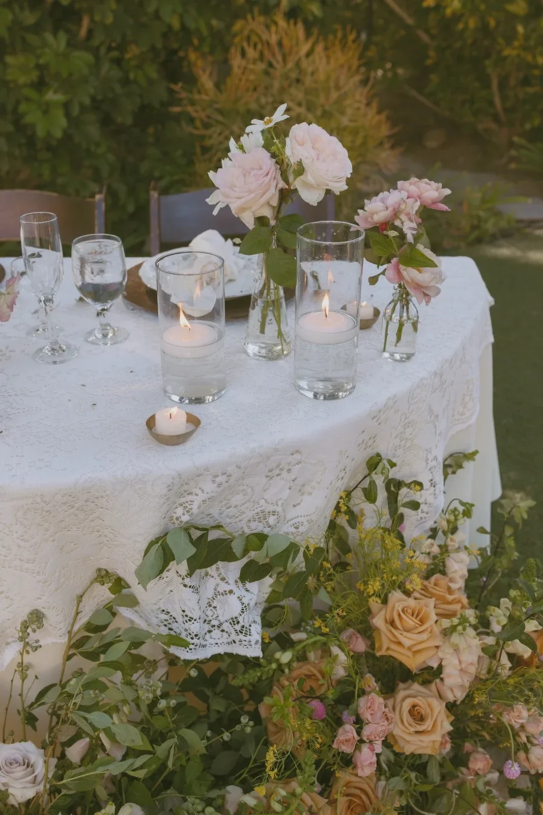 A lace-covered table with roses and candles in a garden at dusk