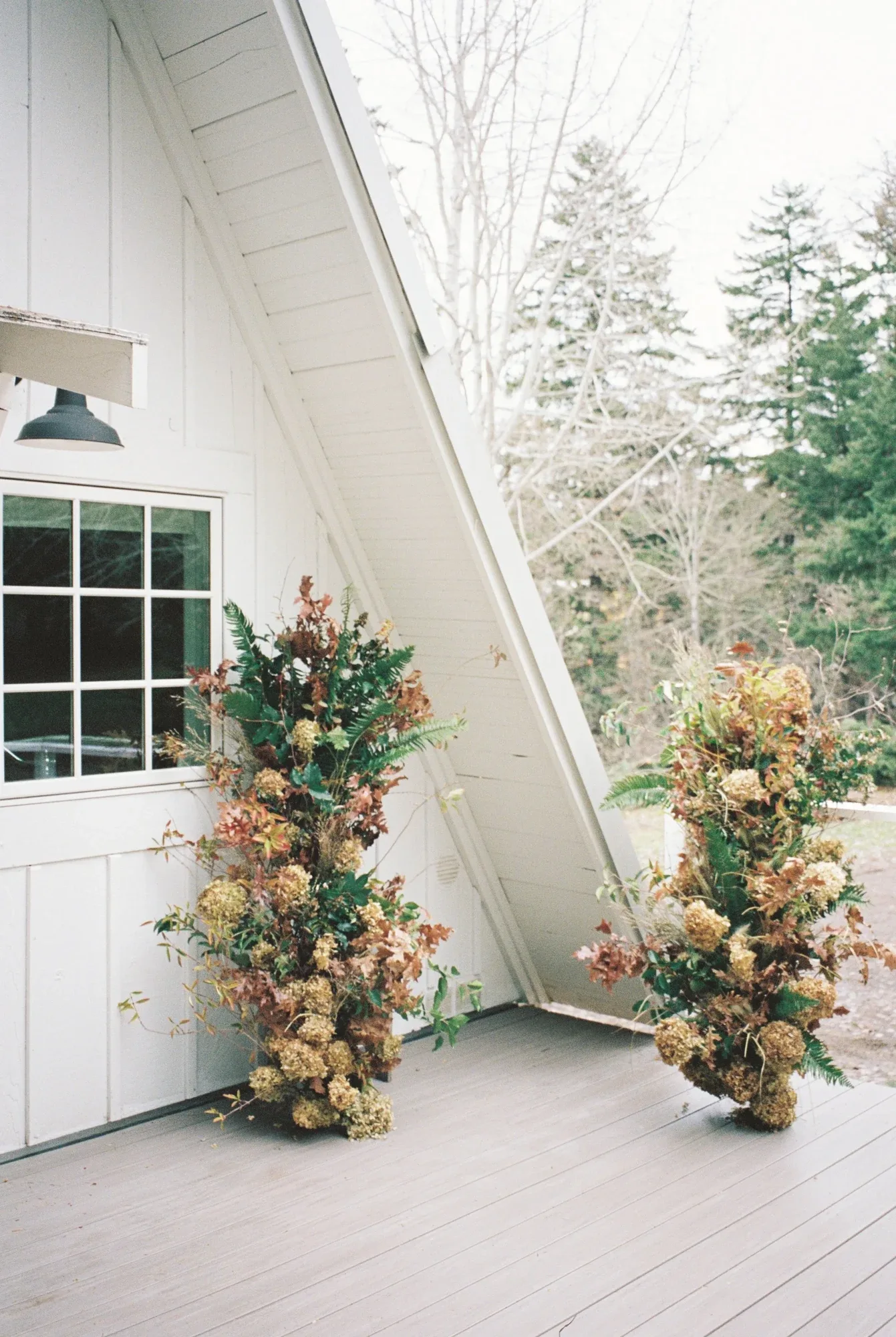 Twin dried-floral columns on the deck of a white A-frame cabin