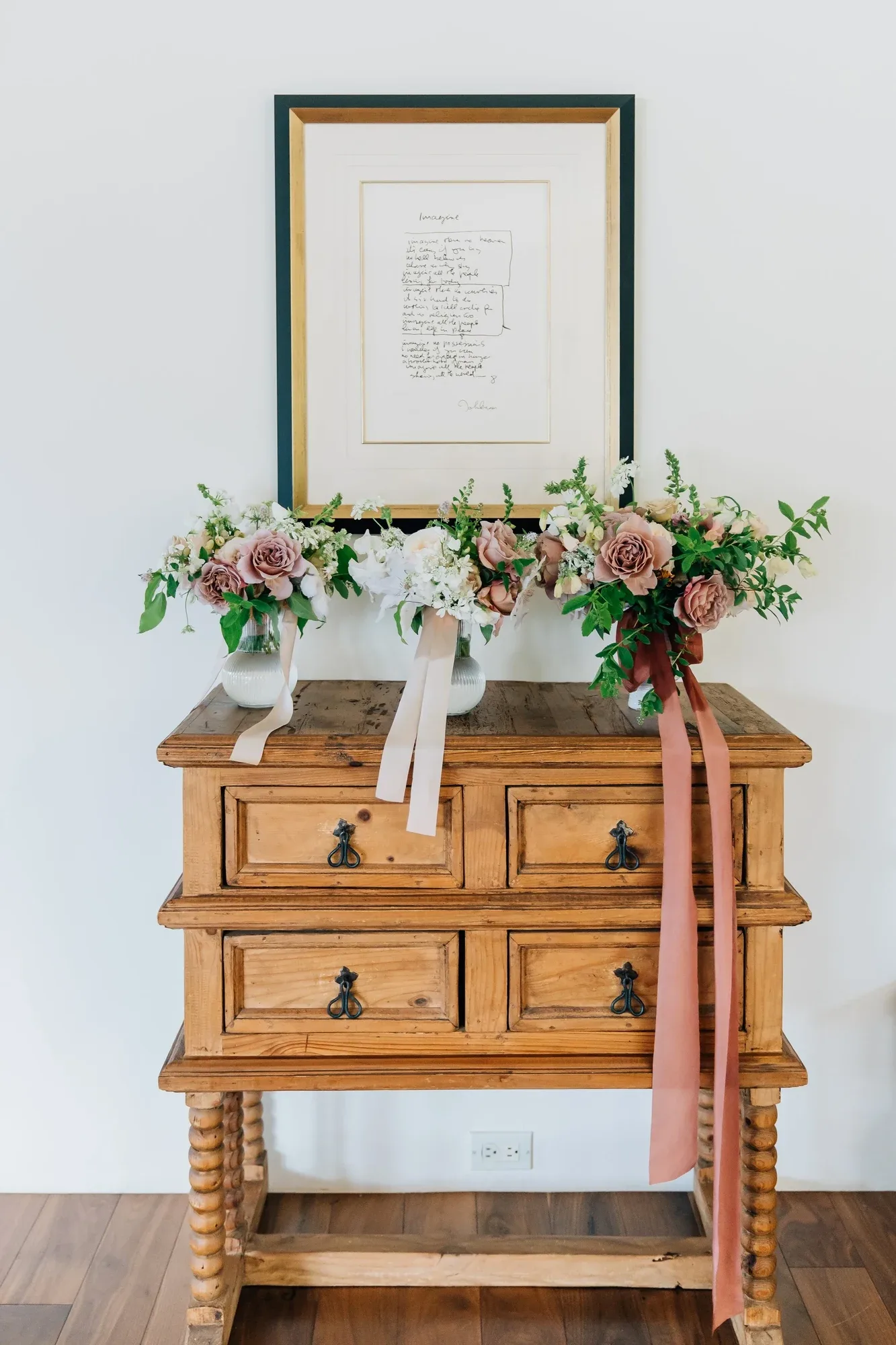 A ribboned floral garland across an antique wooden cabinet beneath a framed letter