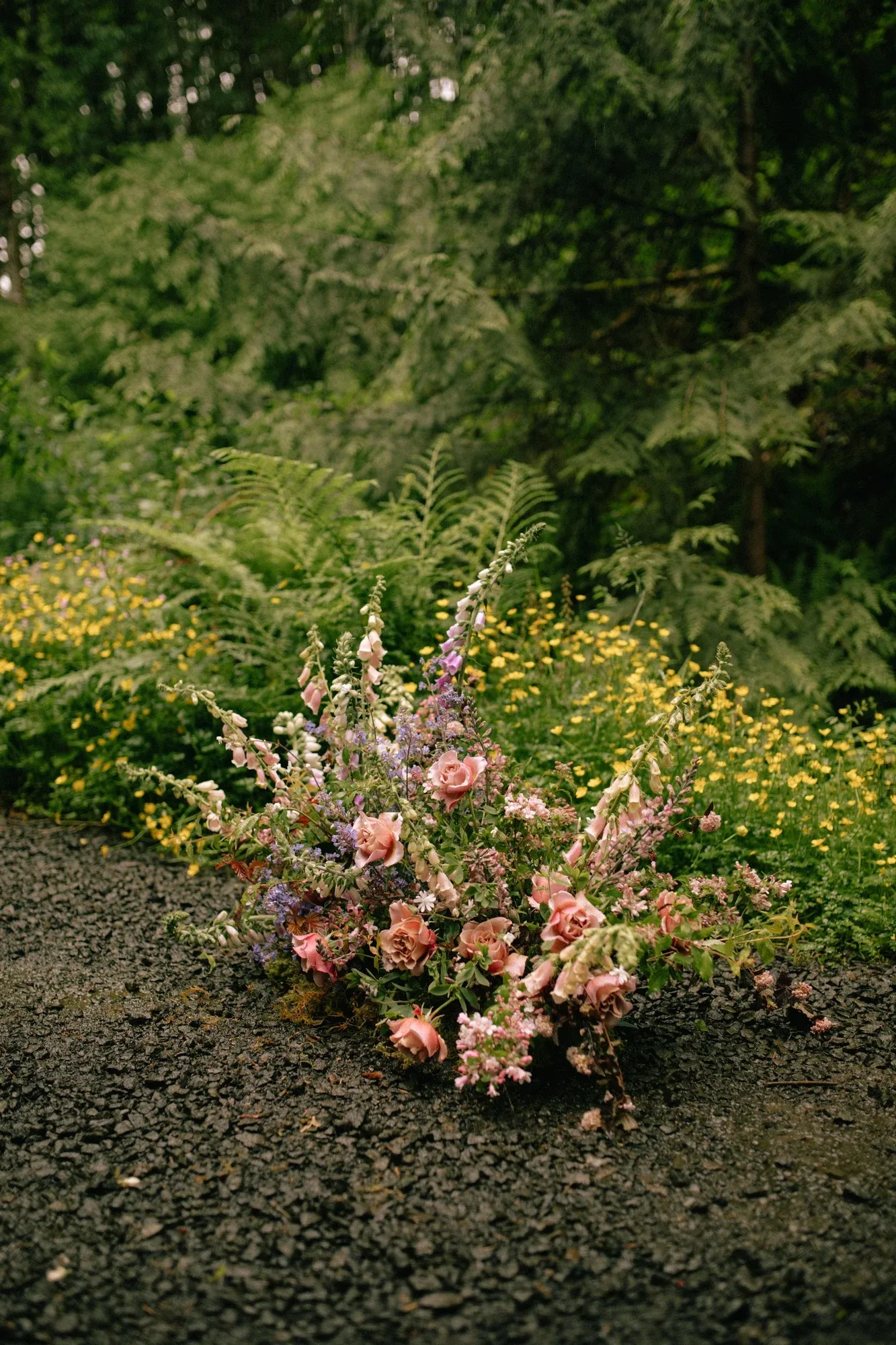 A loose pink and lavender ground arrangement among ferns and yellow wildflowers