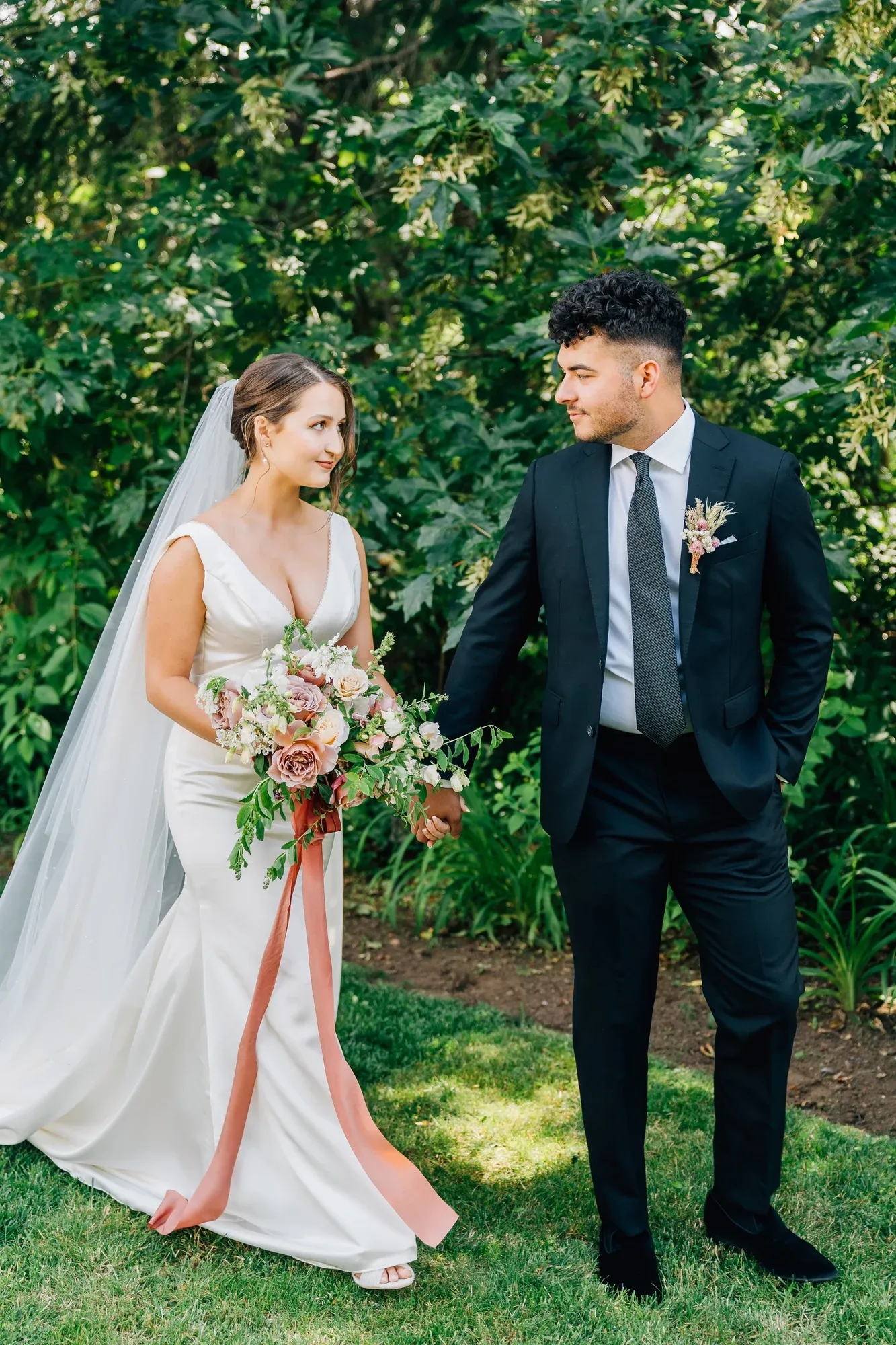 A bride and groom in a garden, the bride holding a bouquet tied with a rust ribbon
