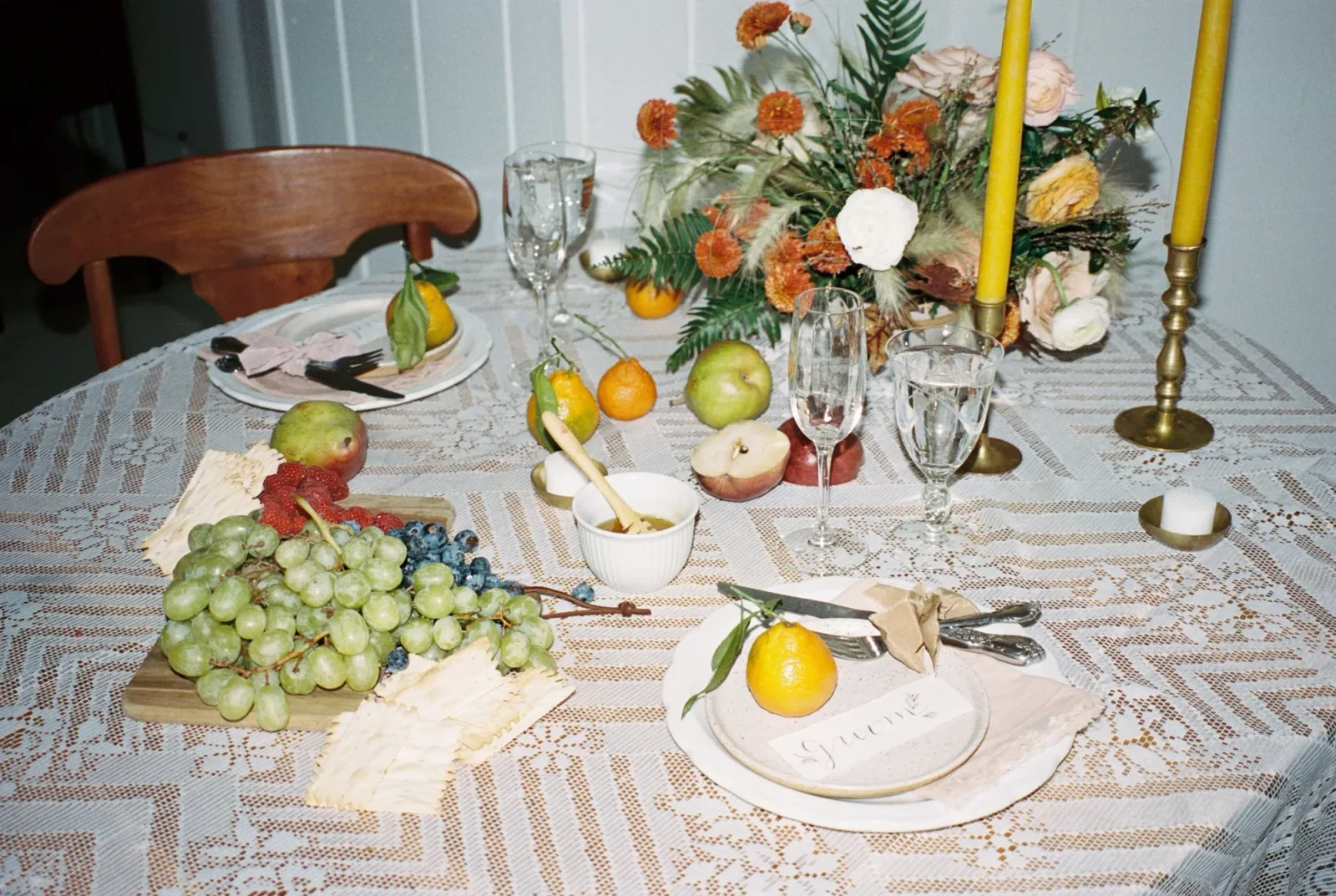 A tablescape of grapes, citrus, orange blooms and tall yellow tapers