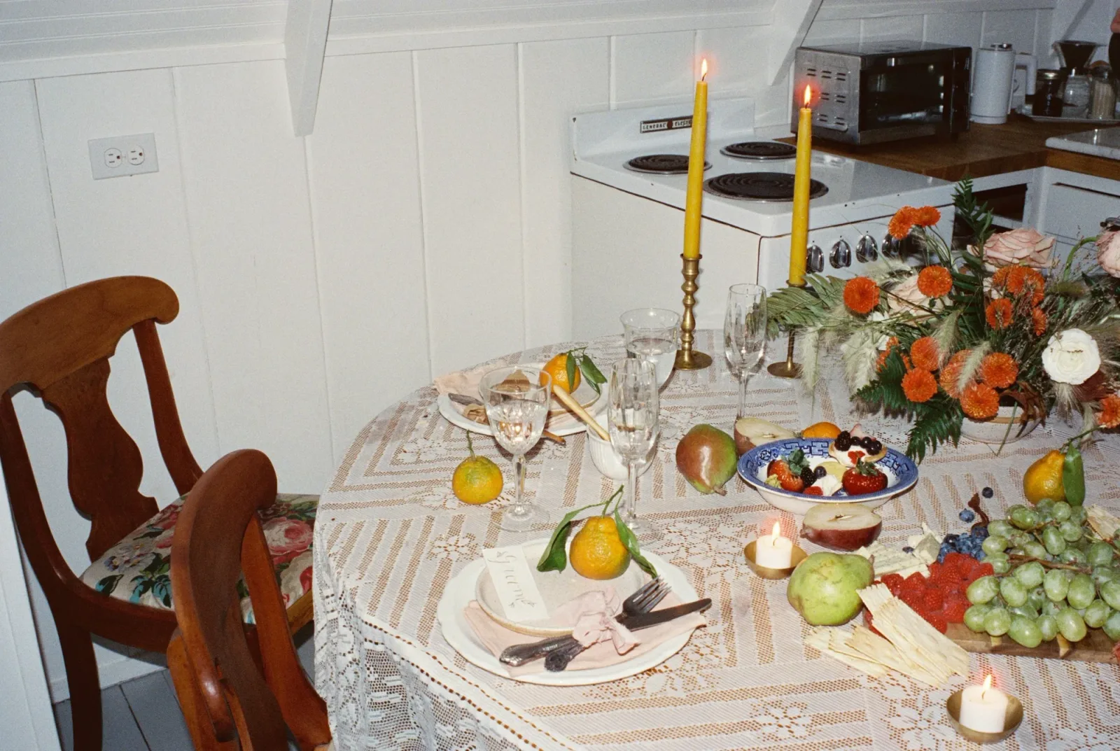 A long table laid with fruit, flowers and yellow tapers in a white kitchen