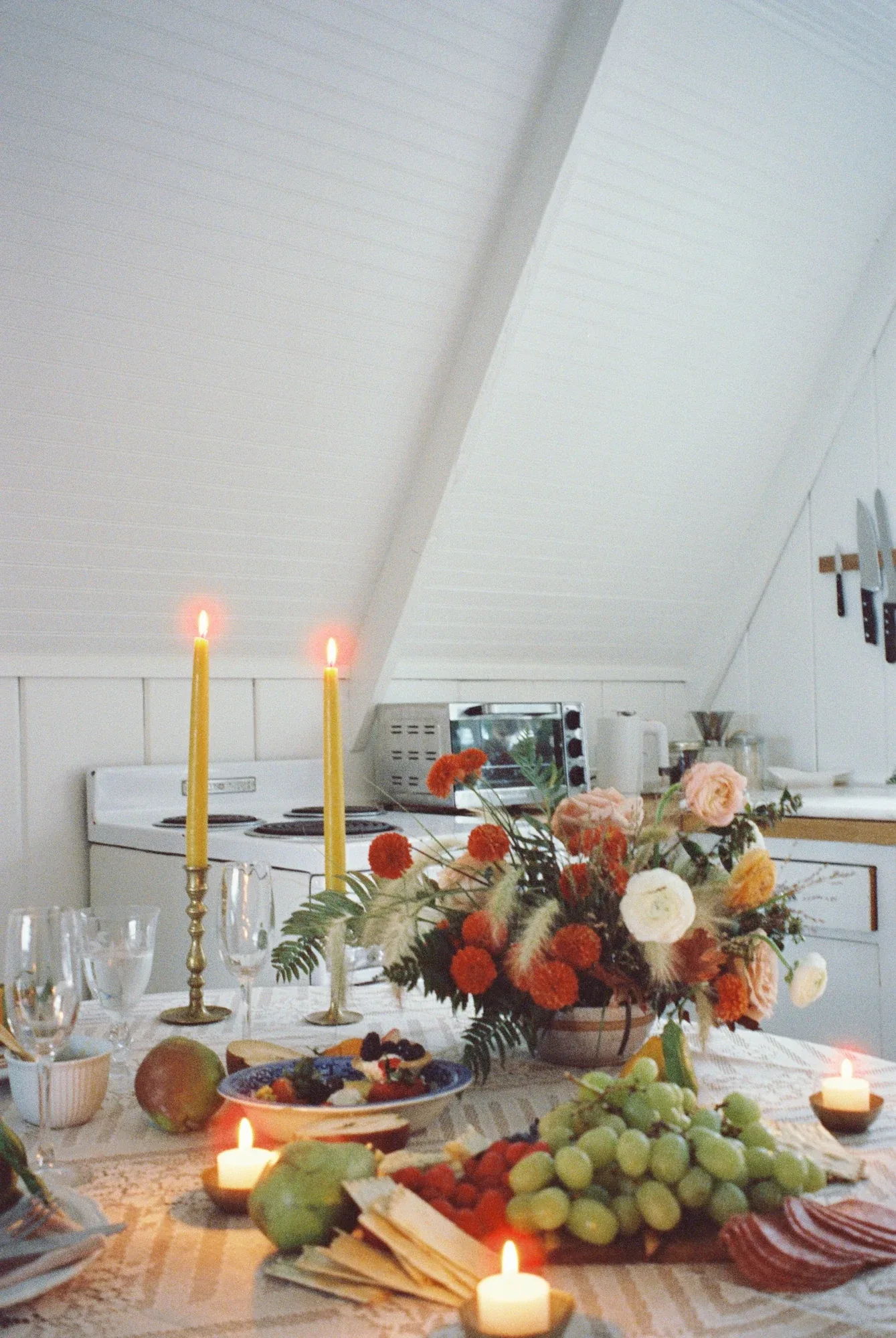 Tall yellow tapers above a fruit-and-flower centerpiece in an A-frame kitchen