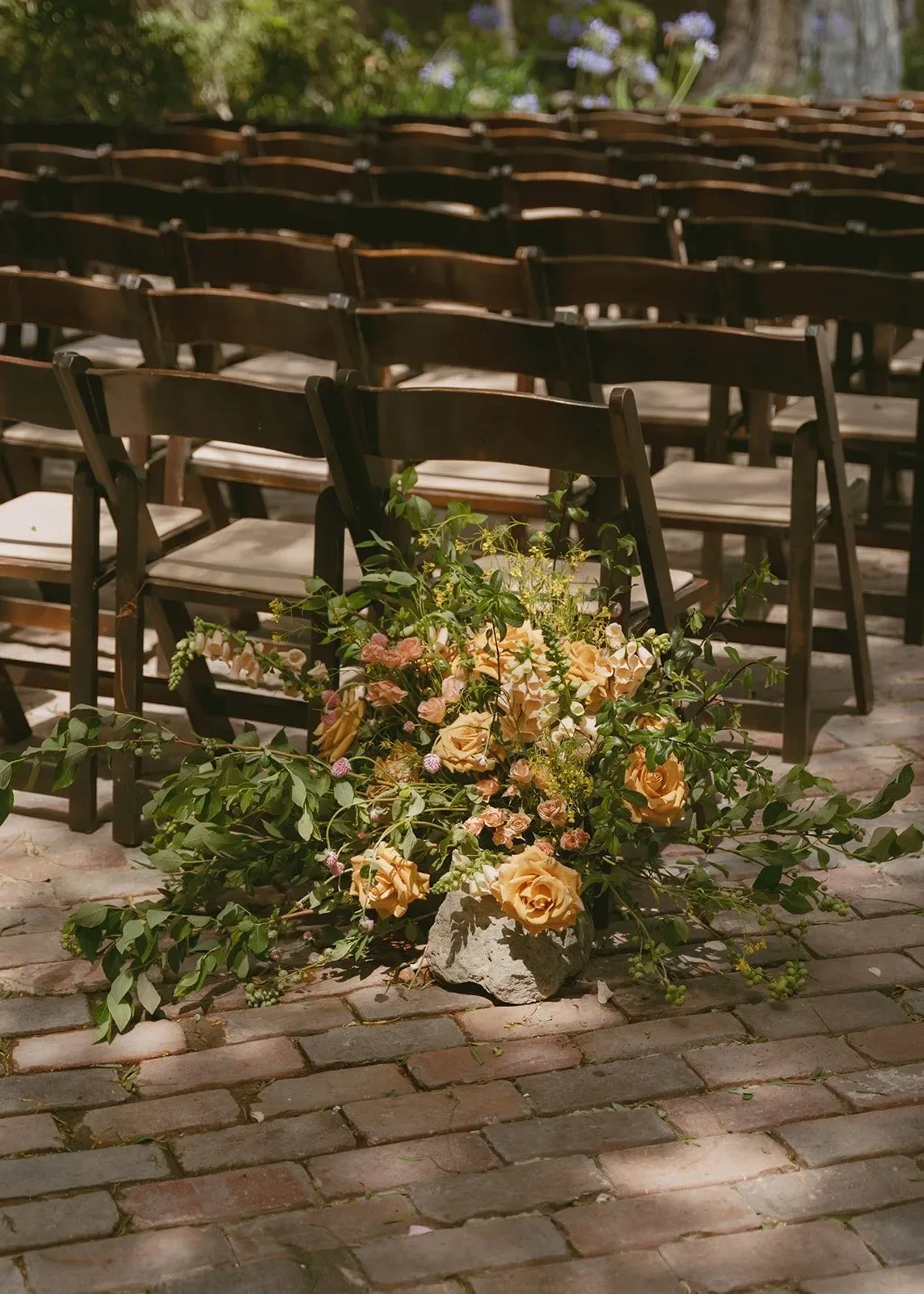 A ground arrangement of peach blooms at the end of a row of wooden chairs